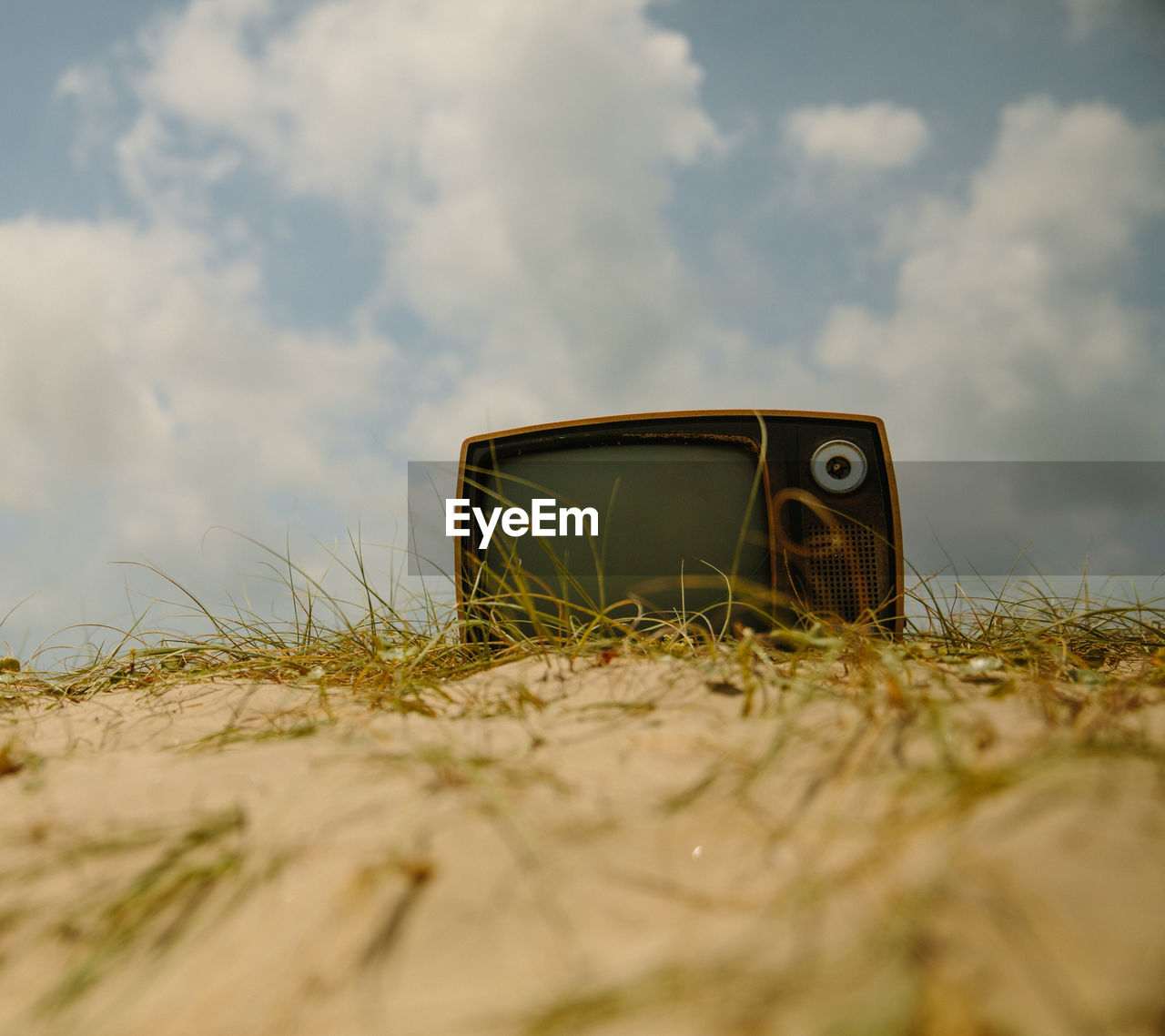 Retro television set on sand against cloudy sky