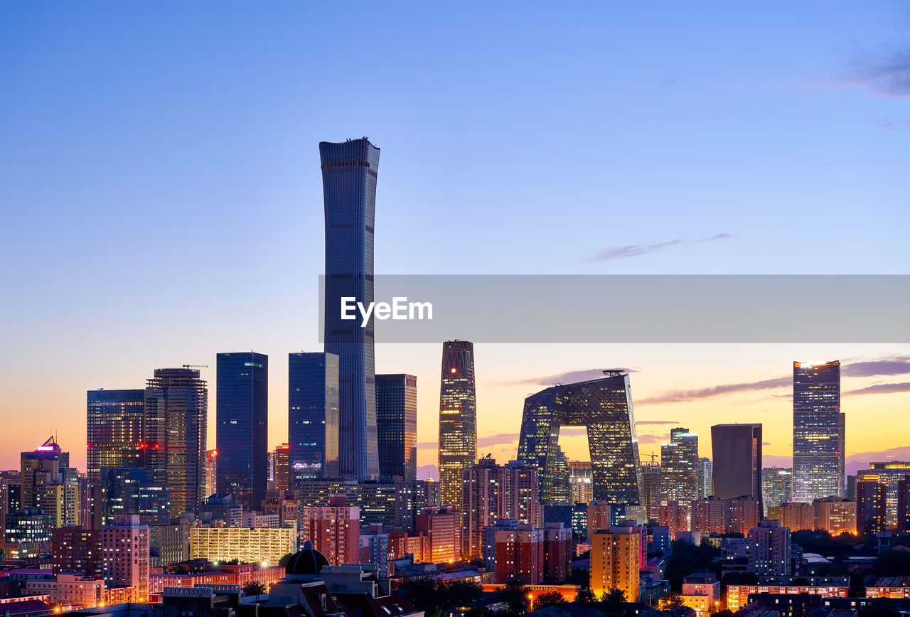 Illuminated buildings in city against sky during sunset