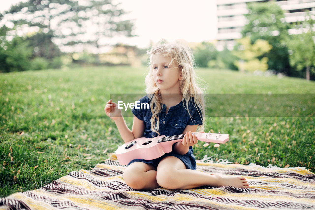 Girl playing pink guitar toy outdoor. child playing music and singing song in park. music hobby 