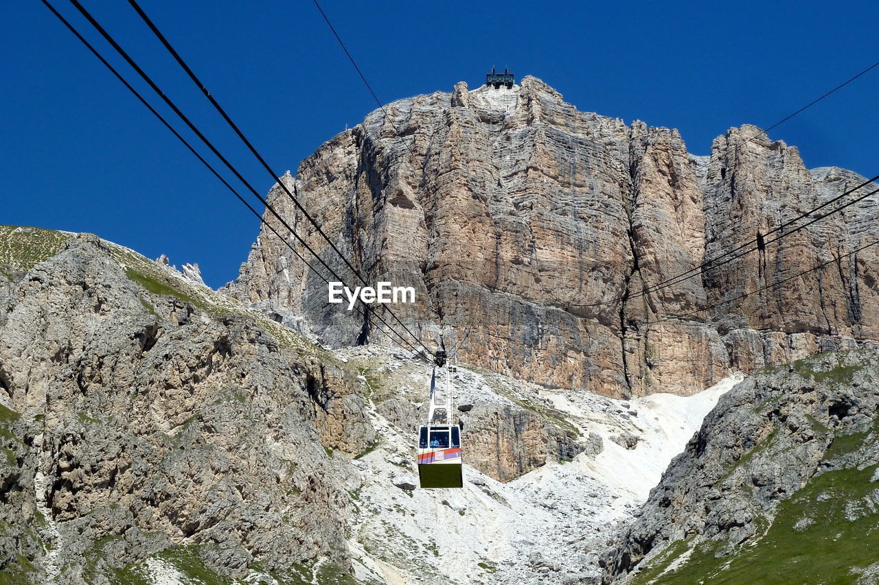 Low angle view of overhead cable car against rocky mountains during sunny day