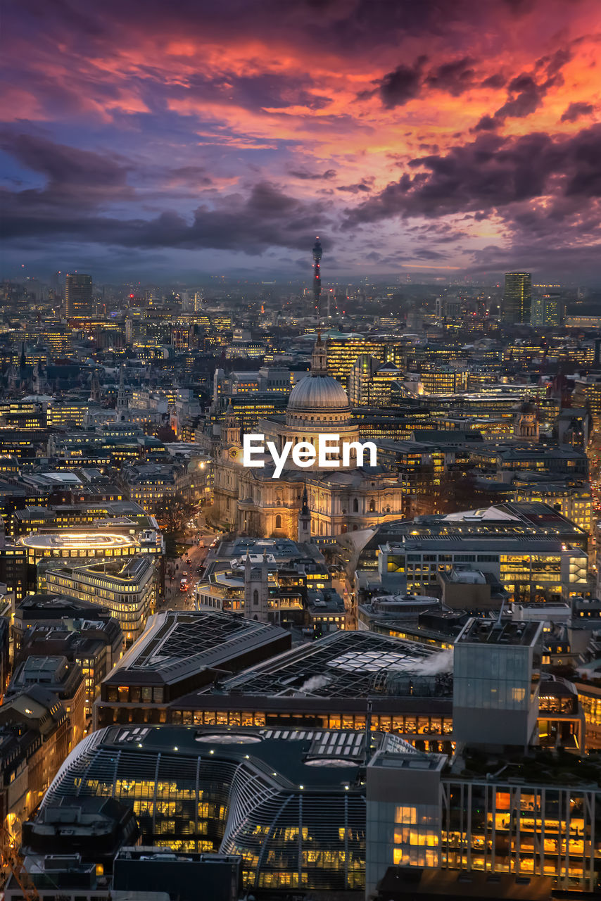 Aerial view of illuminated cityscape against cloudy sky during sunset