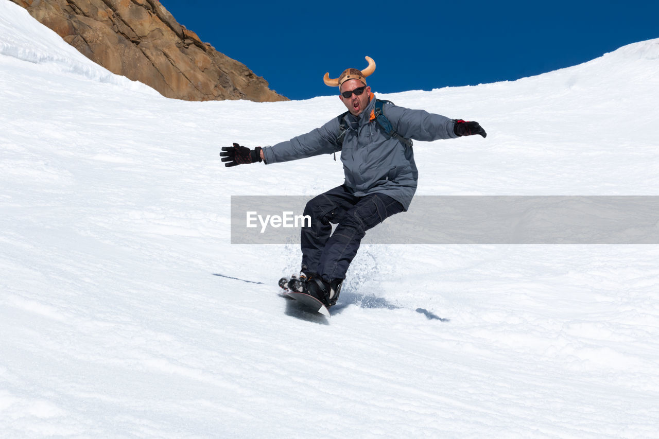 Snowboarder running down the slope in ski resort with a funny hat.