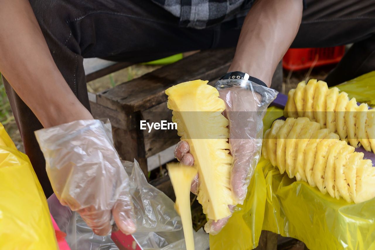 yellow, vegetable, food and drink, food, freshness, healthy eating, midsection, adult, one person, business finance and industry, business, holding, sweet corn, occupation, hand, close-up, produce, plastic, wellbeing, retail, men, fruit, outdoors