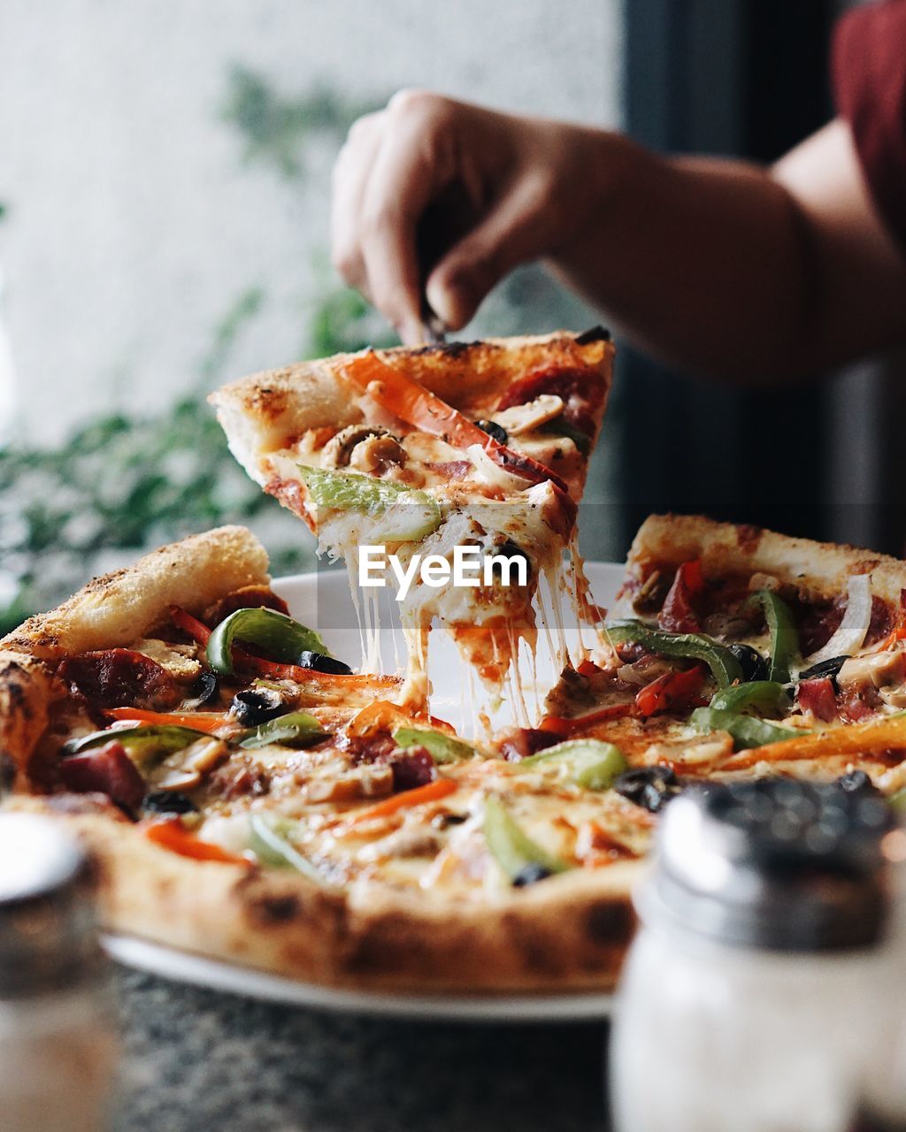 Cropped hand of woman holding pizza slice with server