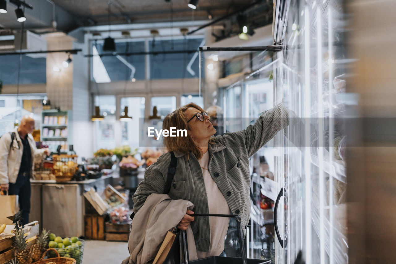 Senior woman reaching for product while doing grocery shopping in supermarket