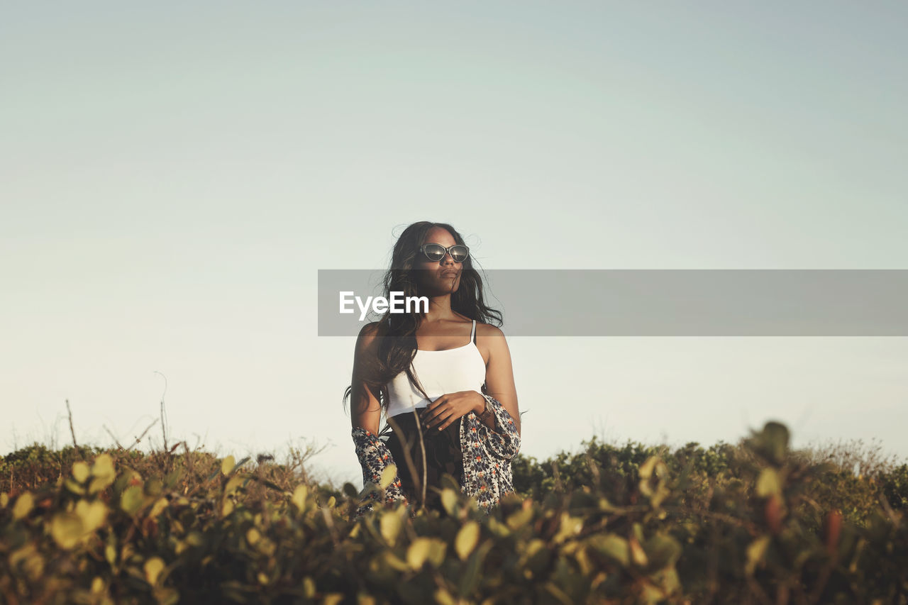 Low angle view of thoughtful young woman sitting on field against clear sky