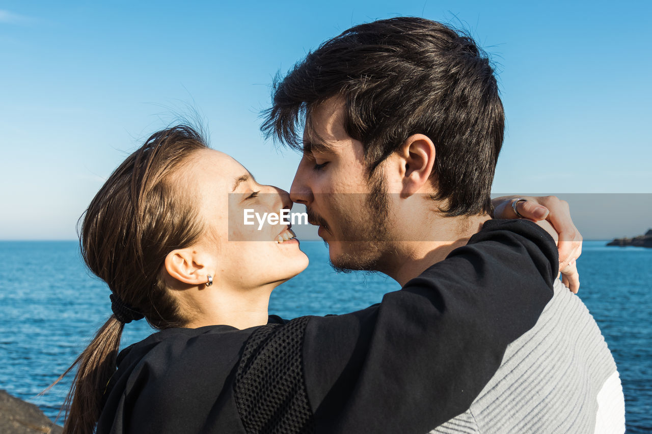 two people, men, adult, togetherness, emotion, water, positive emotion, love, sea, sky, happiness, nature, portrait, young adult, romance, women, ceremony, smiling, headshot, embracing, bonding, beach, blue, vacation, holiday, affectionate, trip, land, leisure activity, casual clothing, person, clear sky, day, lifestyles, outdoors, cheerful, female, enjoyment, summer, sunlight, beauty in nature, travel, brown hair, kissing, relaxation, sunny, side view