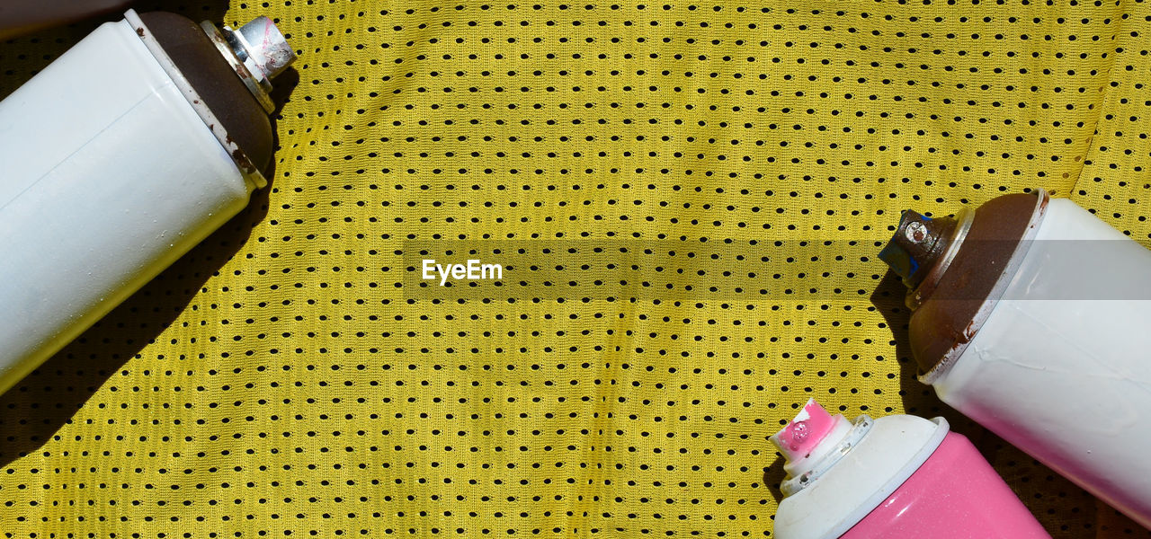 High angle view of spray cans on yellow fabric