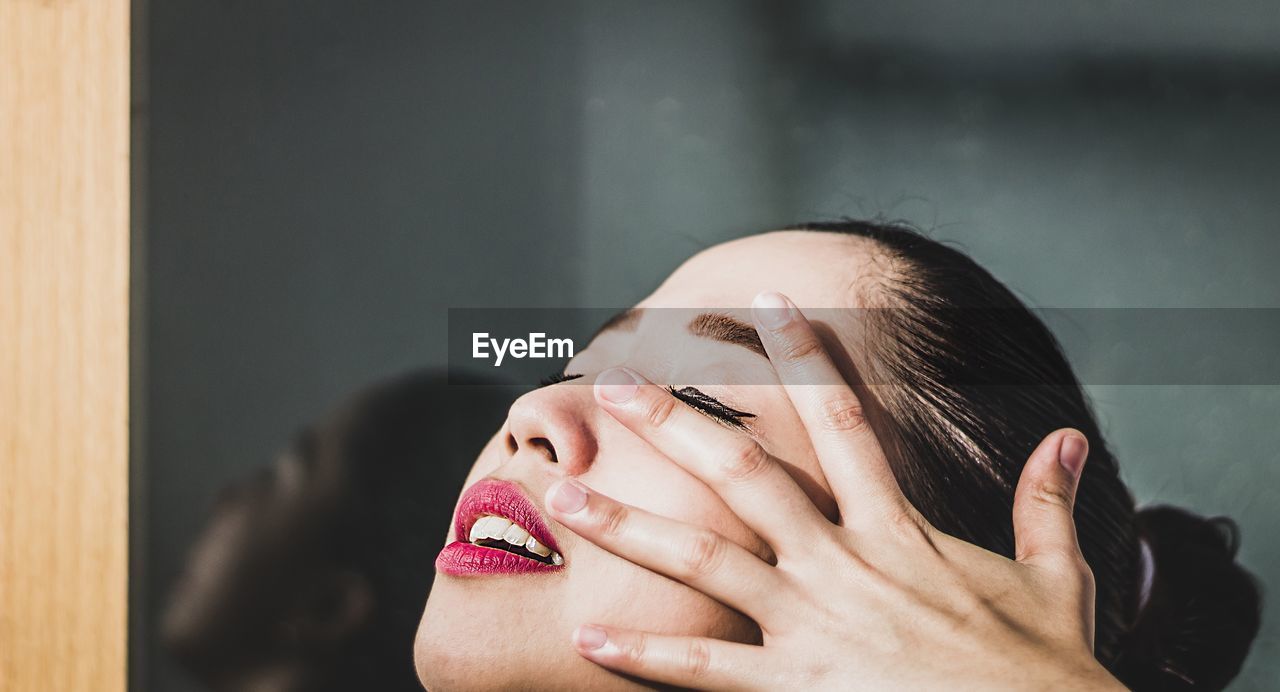 Close-up of young woman touching face by window