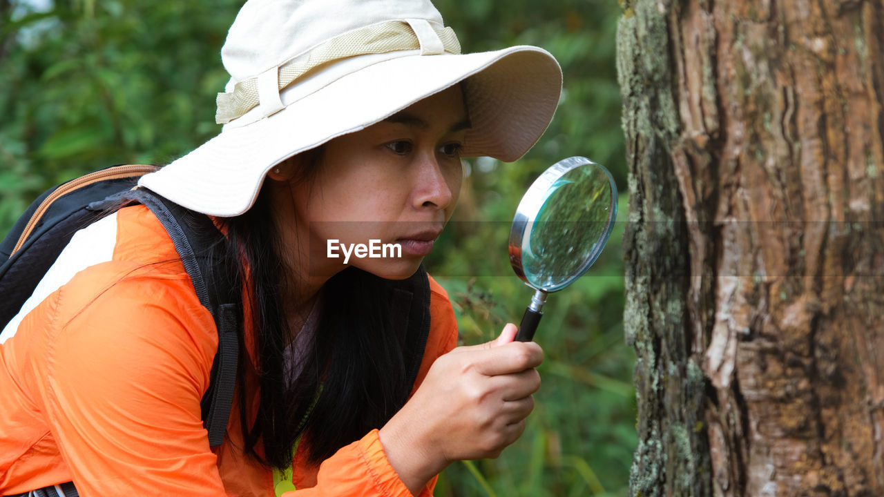 portrait of young woman holding magnifying glass in forest
