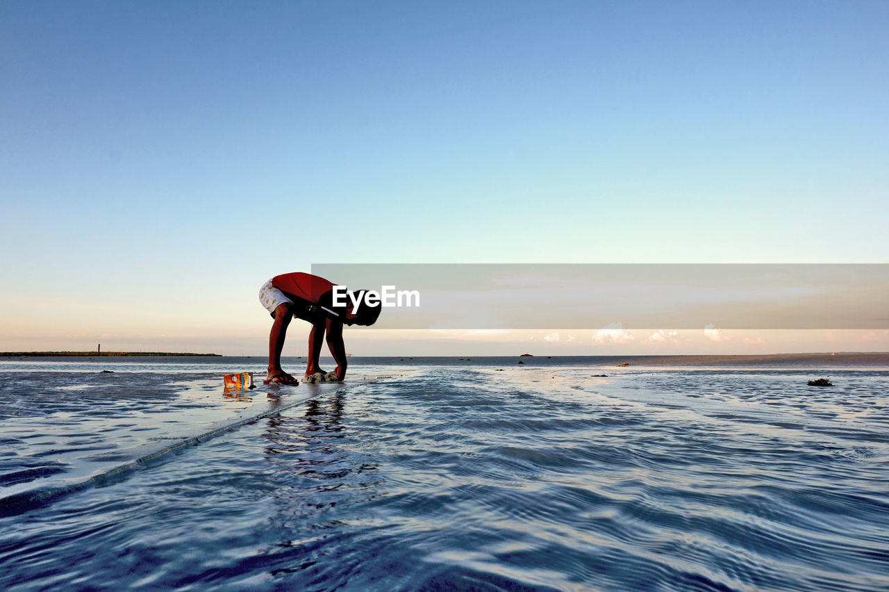 Boy playing on sea shore at beach against clear sky during sunset