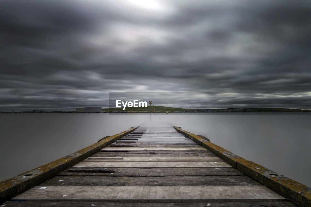 Wooden pier over sea against cloudy sky