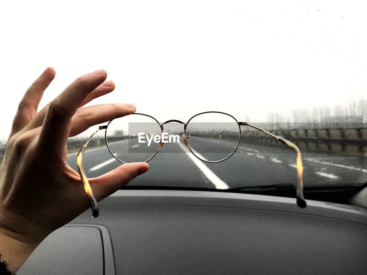 Cropped hand holding eyeglasses in front of car windshield