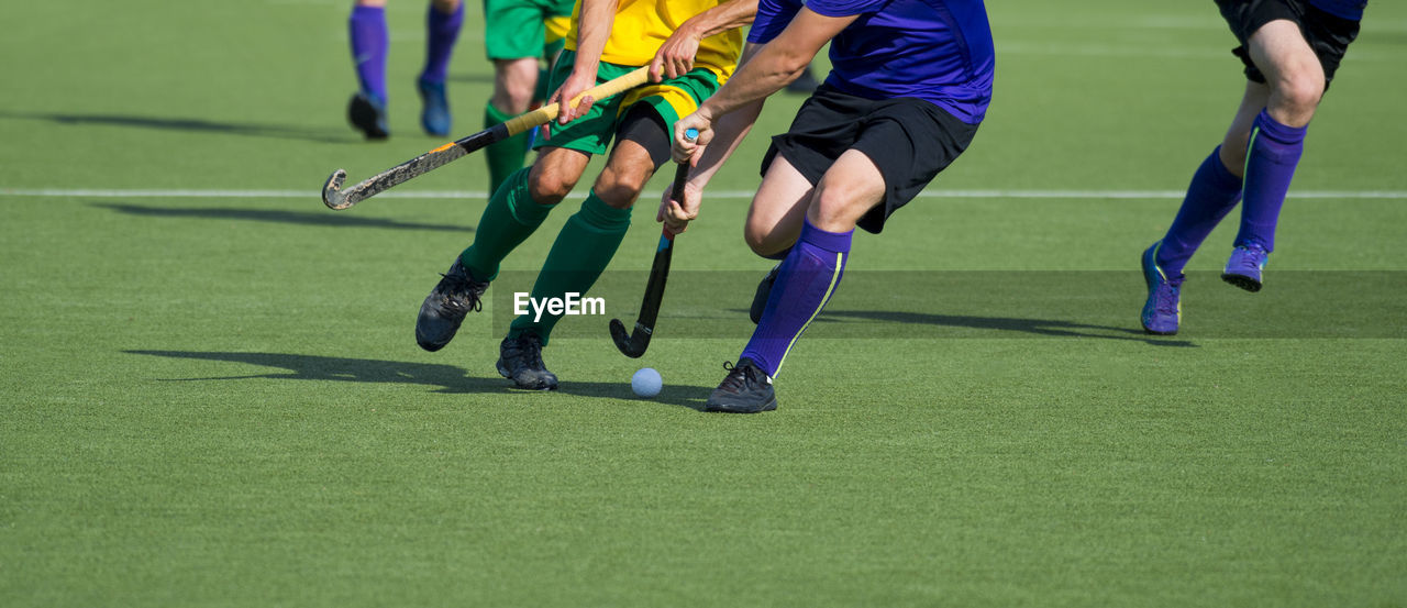 Low section of men playing hockey on turf