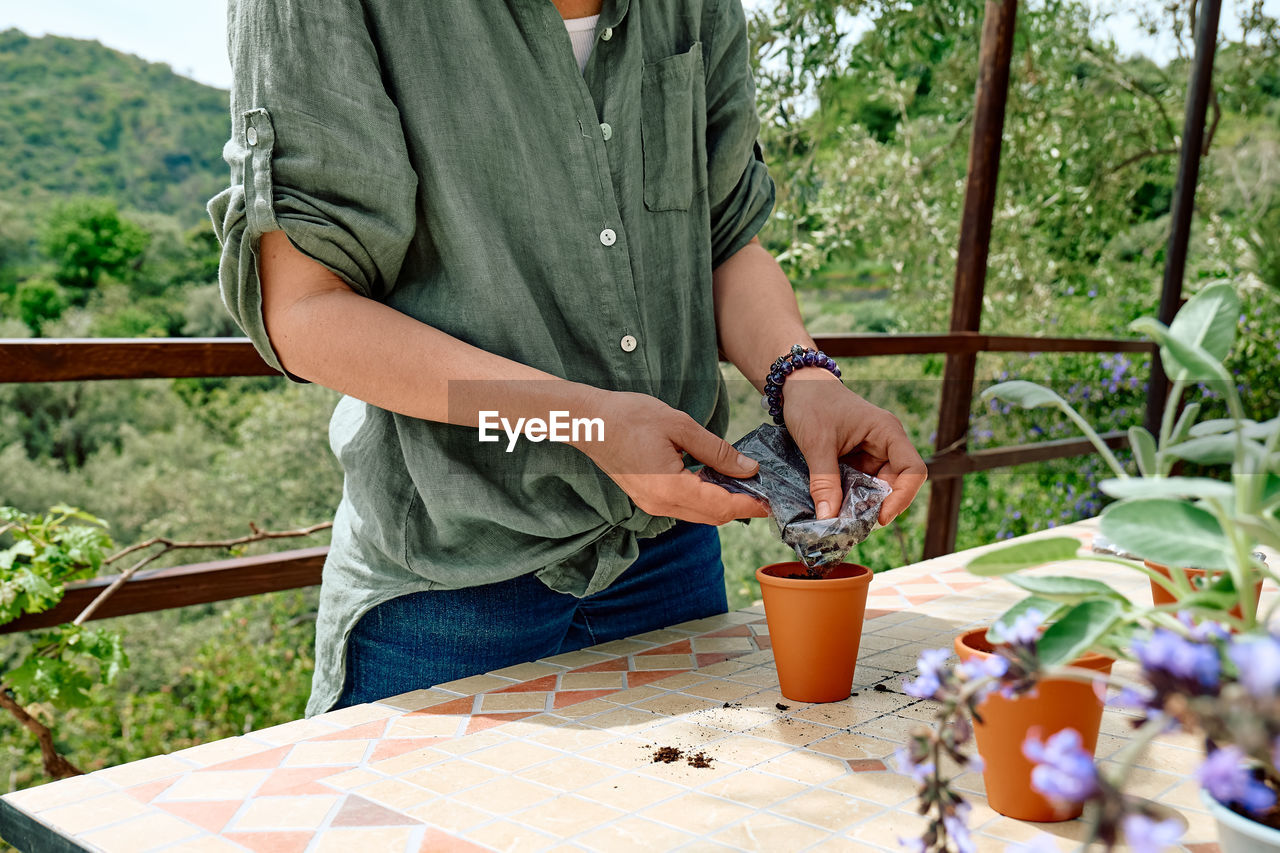 Woman sowing medicinal or aromatic herbs in clay pot on balcony. home planting and food growing. 