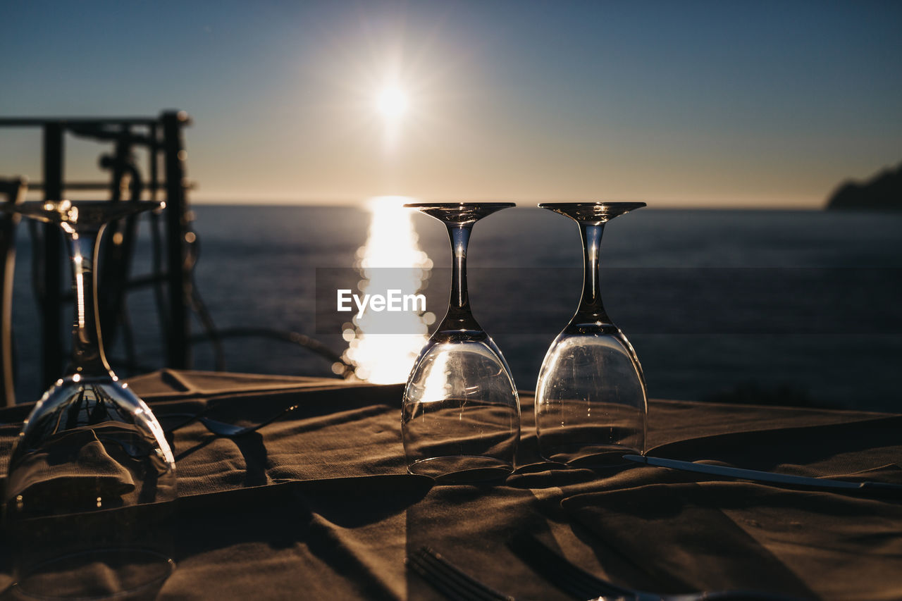 Empty wine glasses on the table by the sea, water and sunset on the background.