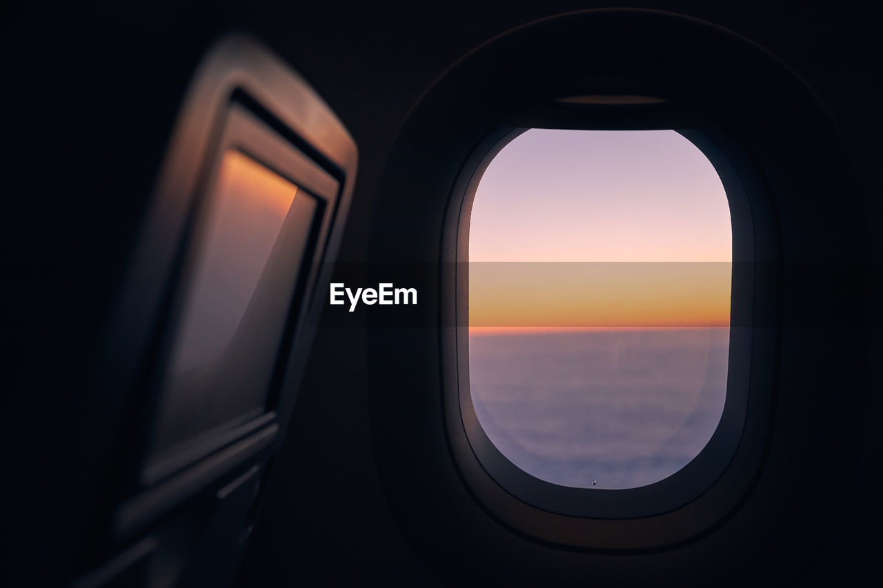 Window of airplane during flight above clouds at beautiful sunset.