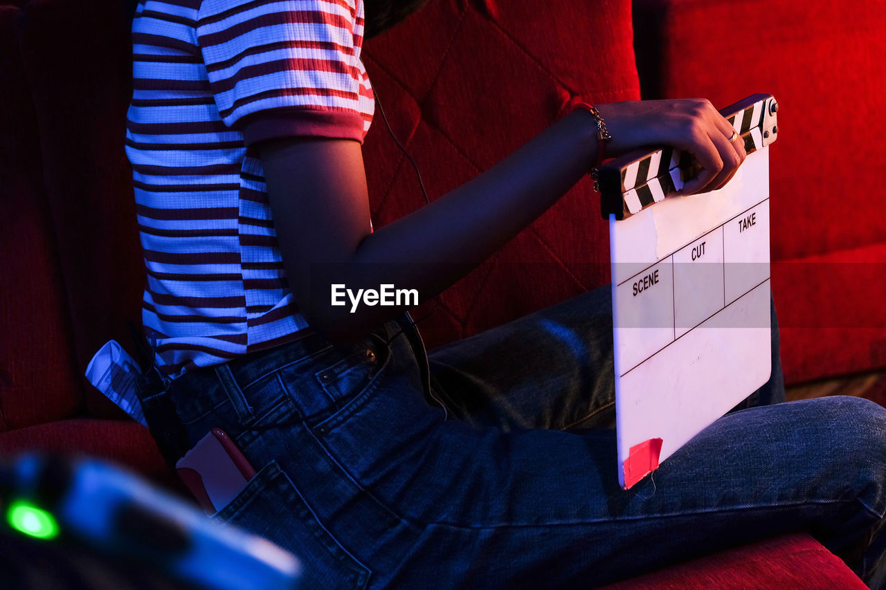 Midsection of woman holding film slate while sitting on chair