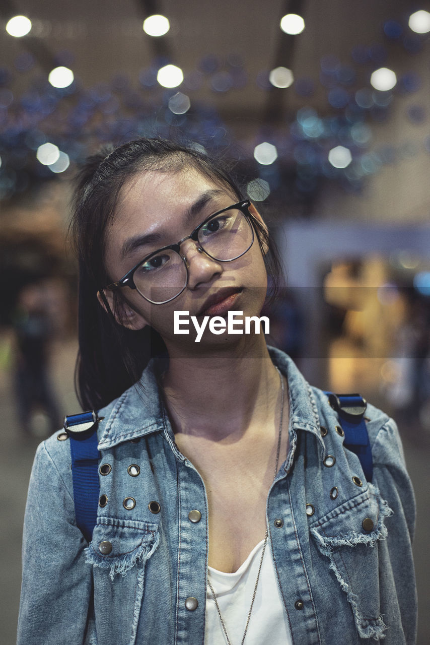 Close-up portrait of teenage girl wearing eyeglasses against defocused lights