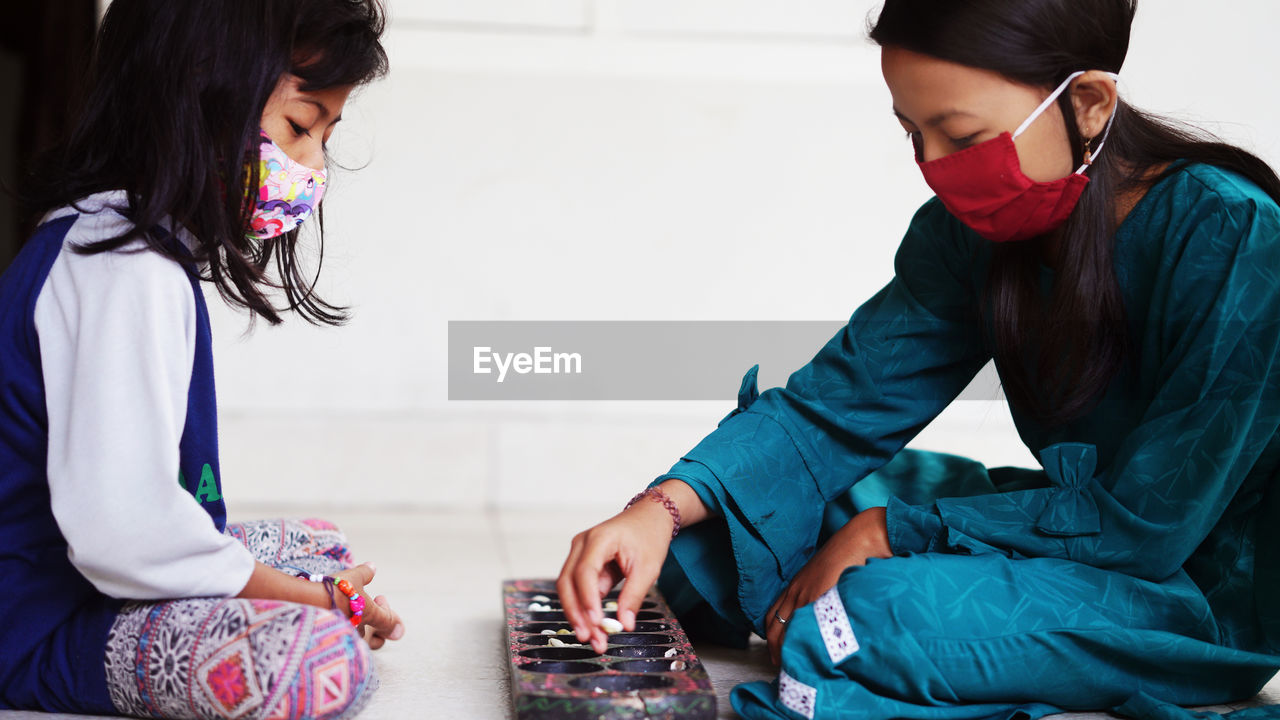 Two girls wearing masks play dakon, a traditional indonesian children's game