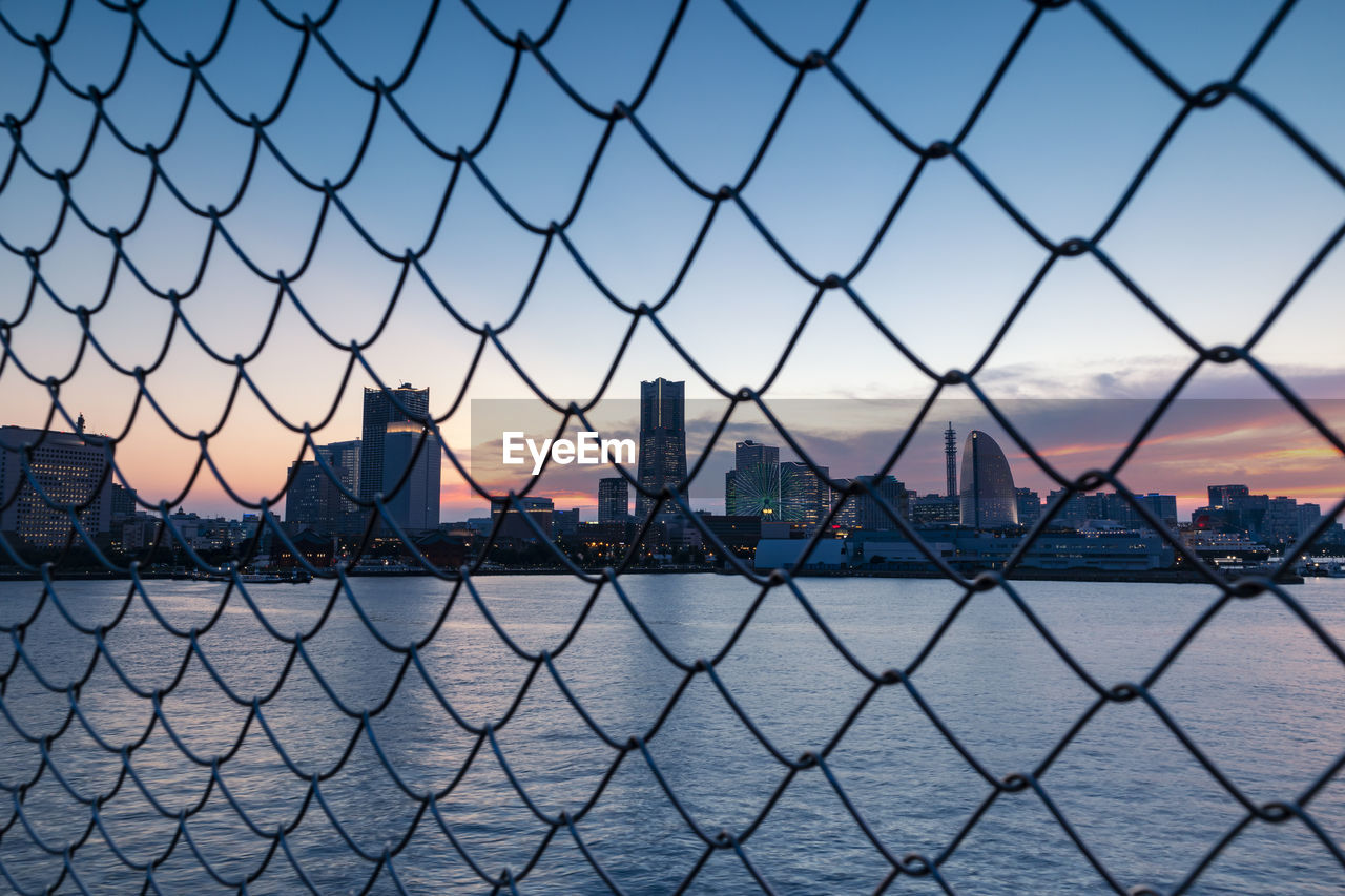 Cityscape by the sea through the grid of fence during sunset. selective focus.