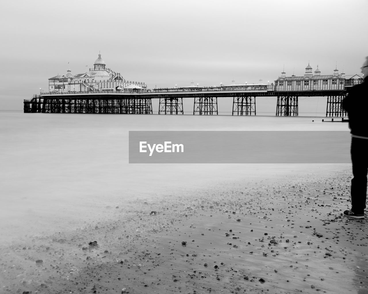 pier, water, black and white, architecture, sky, built structure, monochrome, beach, sea, monochrome photography, nature, land, one person, white, travel destinations, ocean, full length, shore, coast, horizon, tourism, travel, winter, rear view, adult, standing, day, building exterior, men, wave, outdoors, scenics - nature, lifestyles, beauty in nature, snow, sand, holiday, vacation, trip, leisure activity, walking, tranquility, city, morning