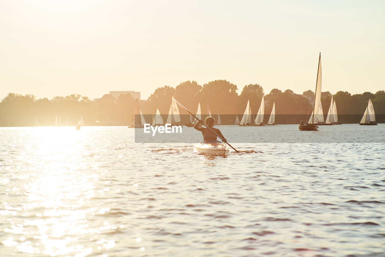 Mid adult woman canoeing on sea against clear sky during sunset