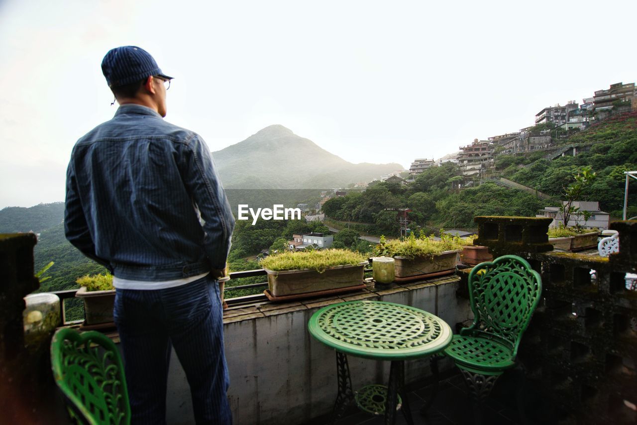 Rear view of man looking at mountains against clear sky