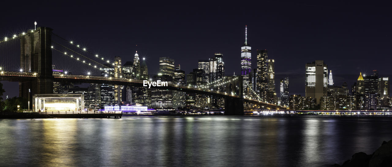 ILLUMINATED BRIDGE OVER RIVER WITH BUILDINGS IN BACKGROUND