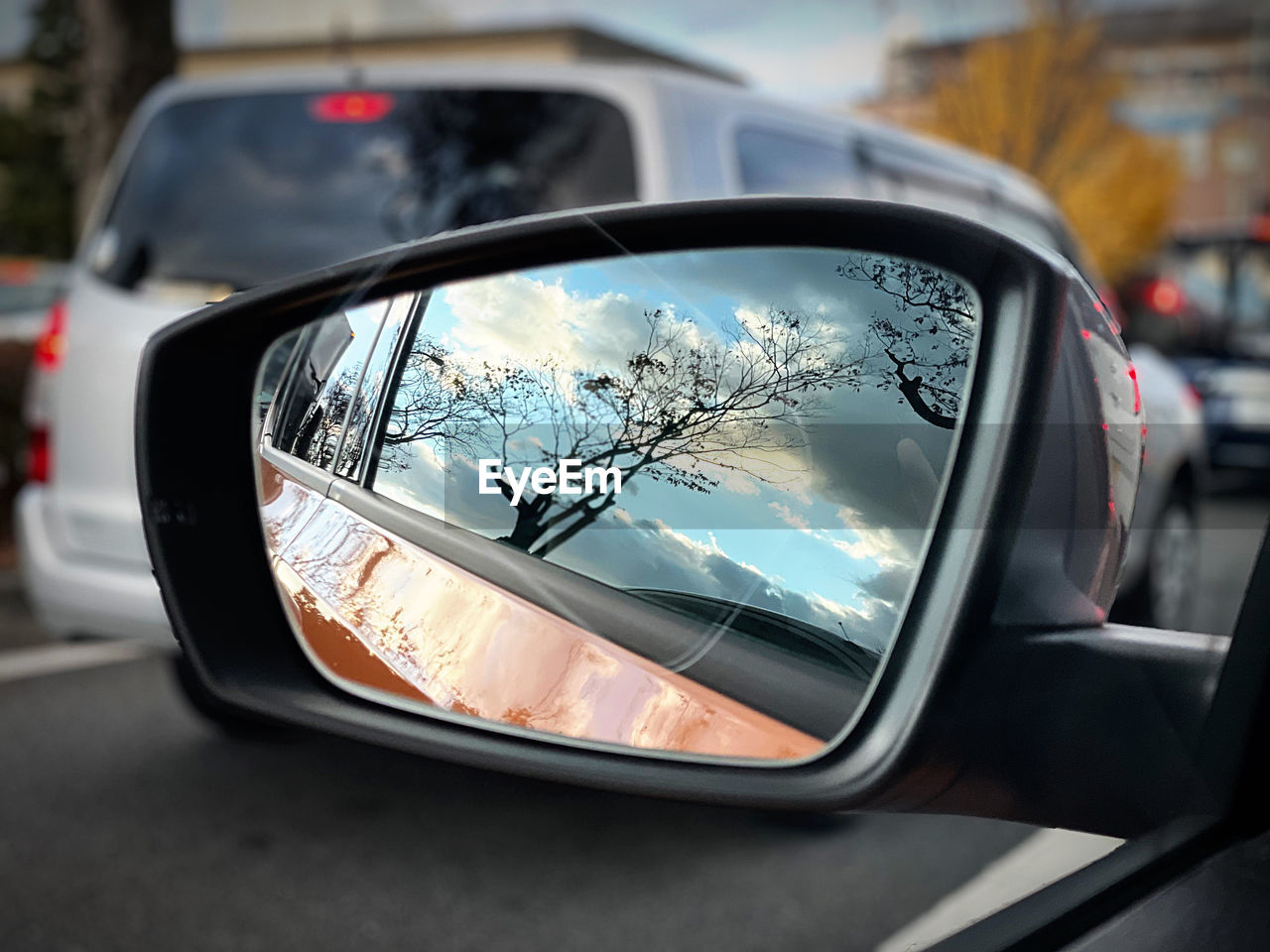 car, motor vehicle, mode of transportation, transportation, vehicle, reflection, side-view mirror, mirror, land vehicle, road, city, automobile, rear-view mirror, vehicle mirror, focus on foreground, travel, glass, street, outdoors, luxury vehicle, close-up, driving, architecture, tree, auto part, automotive exterior, nature, day, automotive mirror, traffic, window, sky, motion