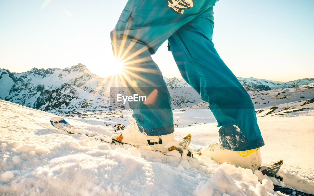 Low section of person hiking on snowcapped mountain against clear sky