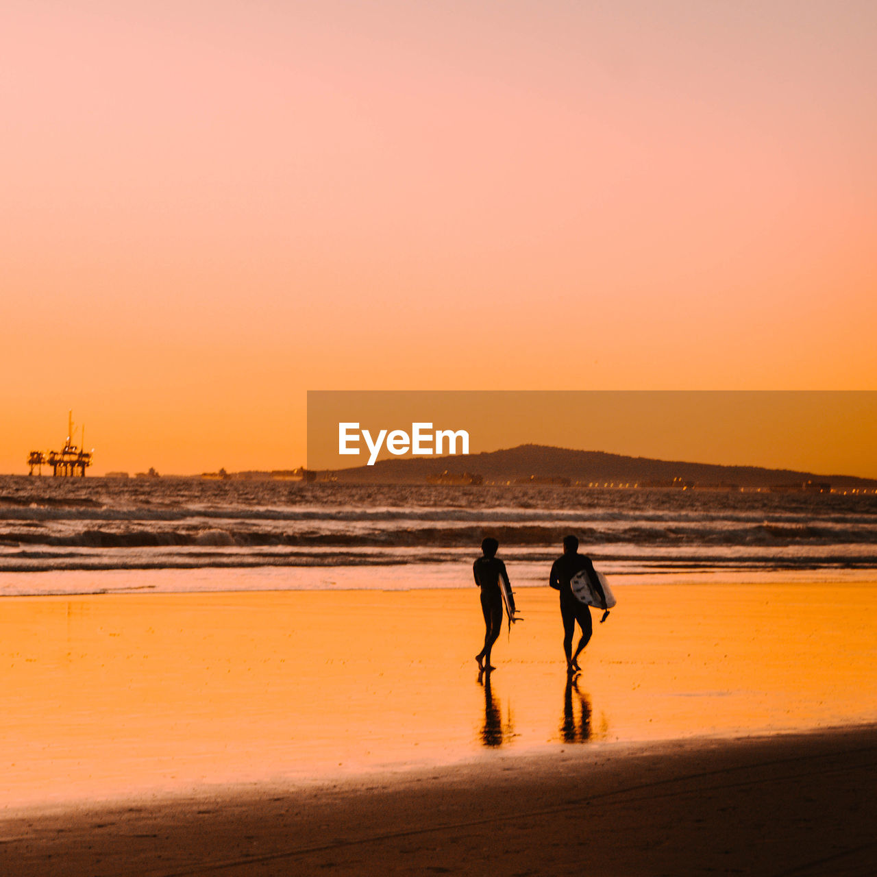 Men walking on beach against sky during sunset