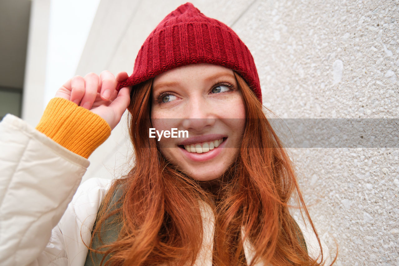 portrait of smiling young woman wearing hat against wall