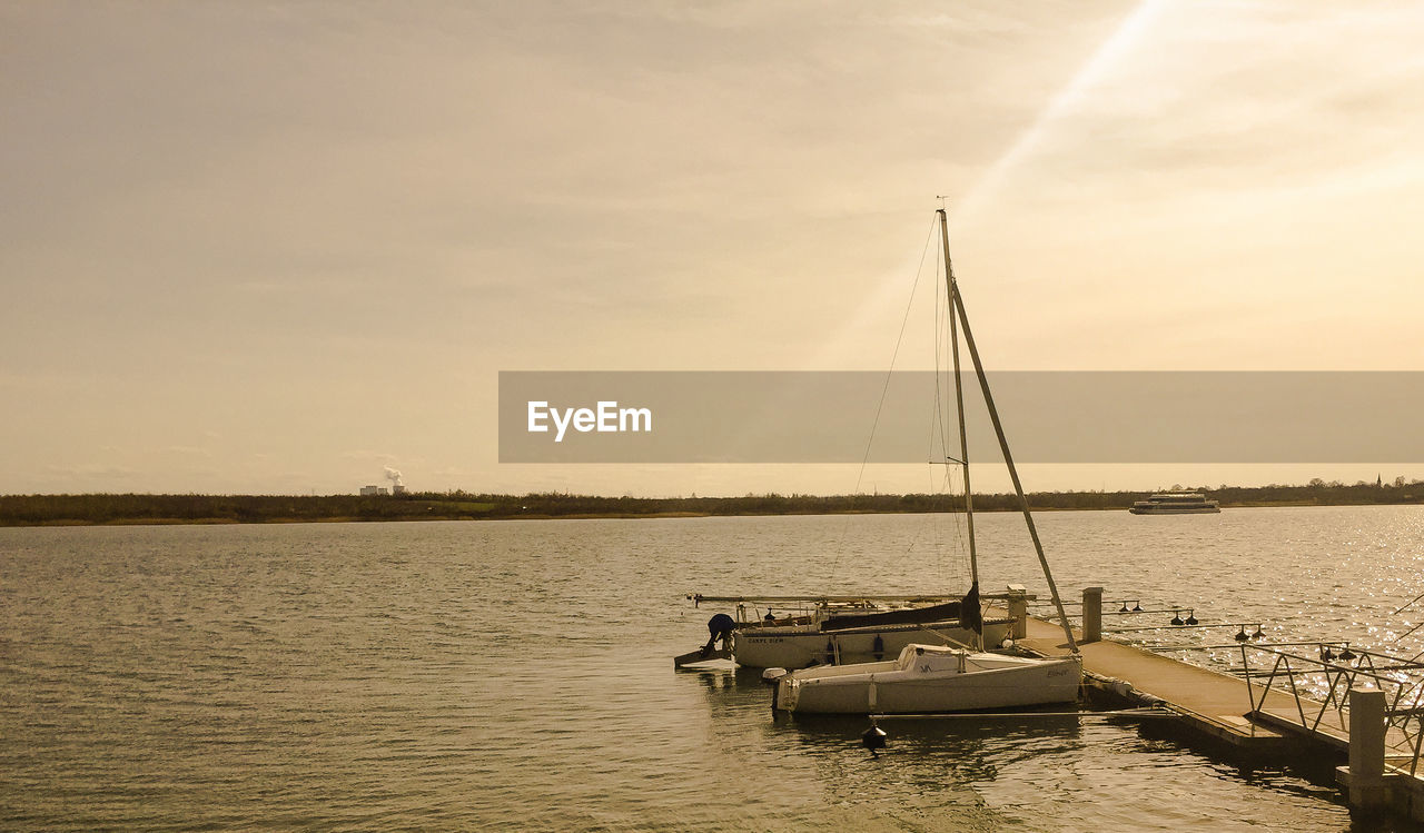 Sailboats moored on sea against sky during sunset