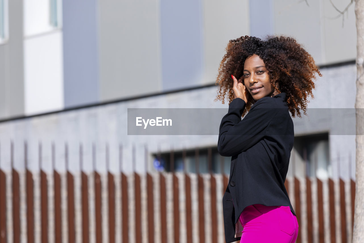 Side view portrait of young woman standing against building in city