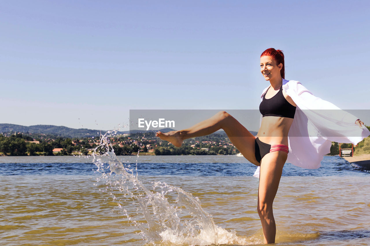 Playful woman having fun in summer day and splashing water at the beach.