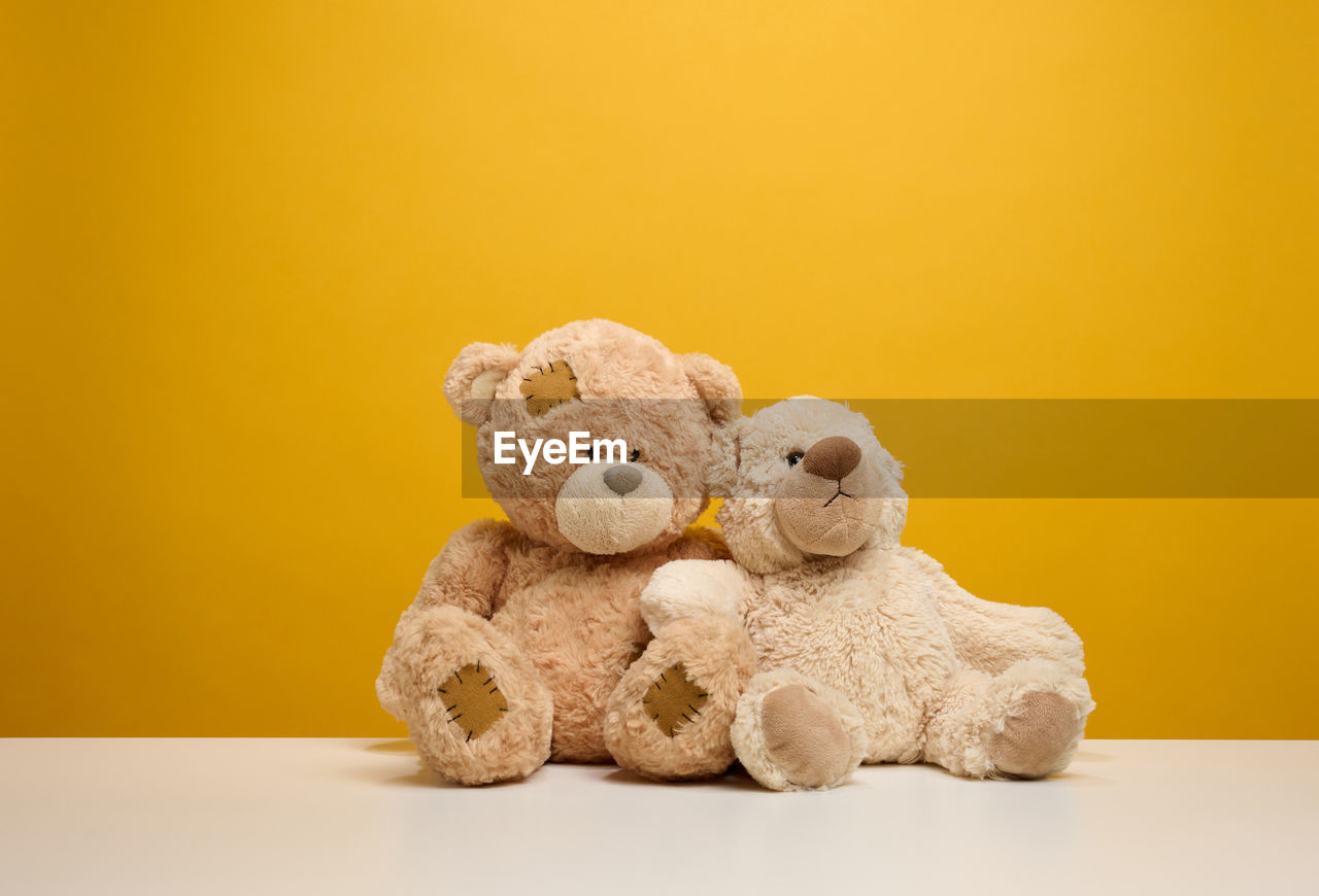 Two cute brown teddy bears sitting on a yellow background, childrens toy