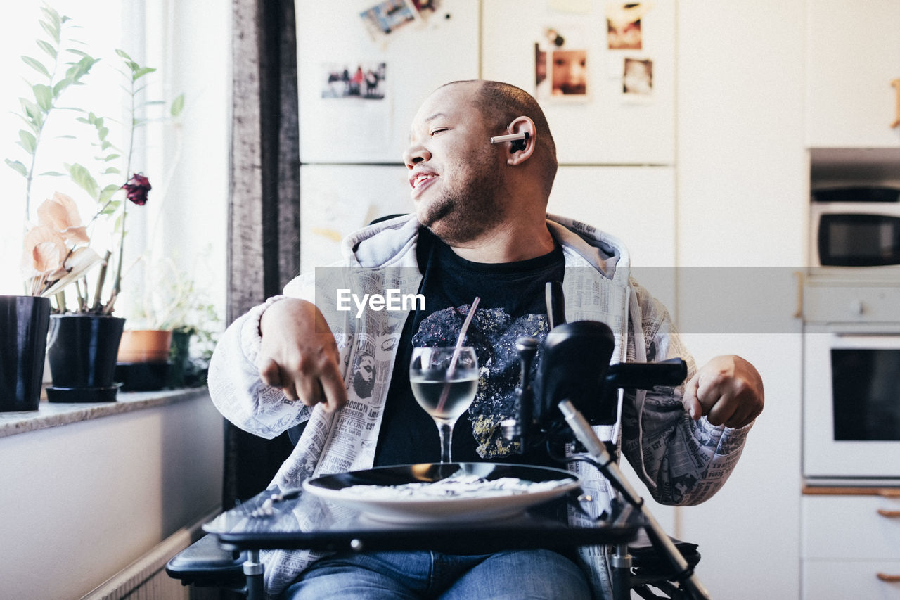 Happy disabled musician with drink sitting by window at recording studio