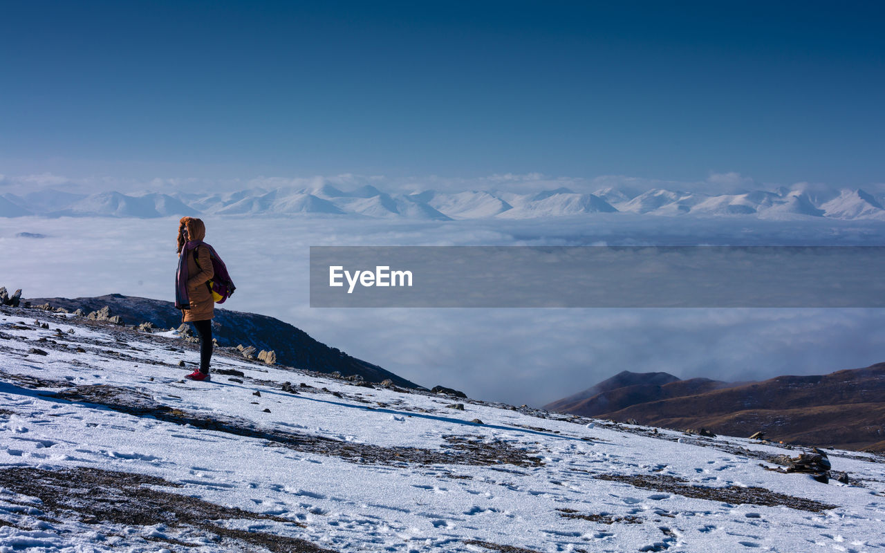 FULL LENGTH REAR VIEW OF WOMAN STANDING ON SNOWCAPPED MOUNTAIN