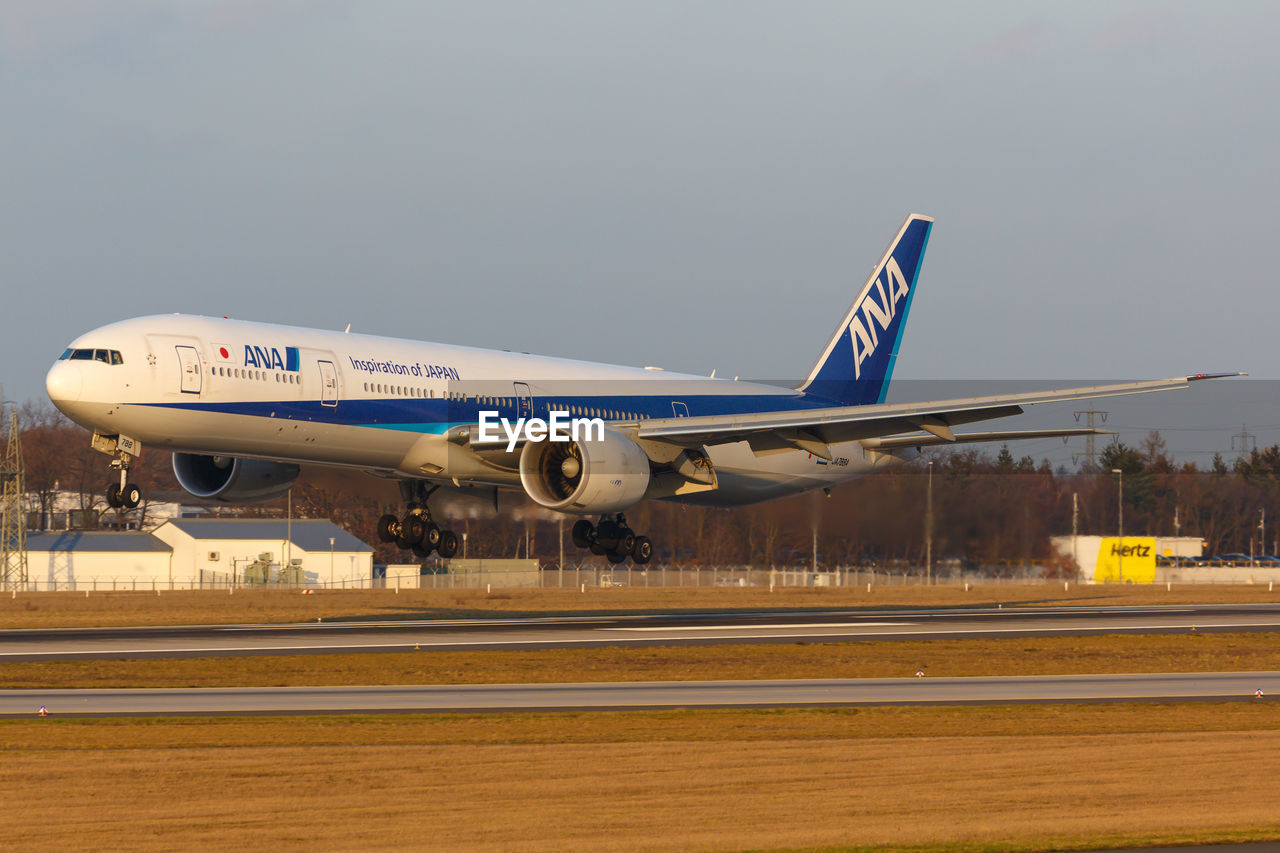 AIRPLANE FLYING OVER RUNWAY AGAINST SKY