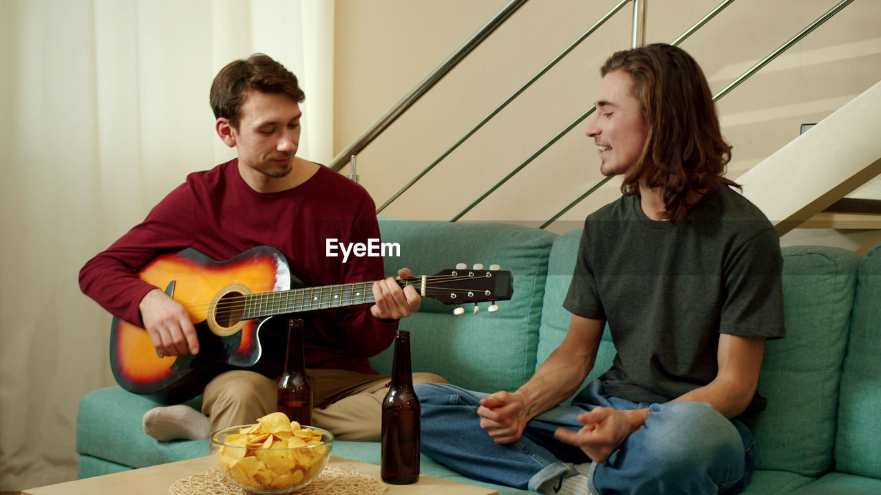 Homosexual couple playing guitar at home