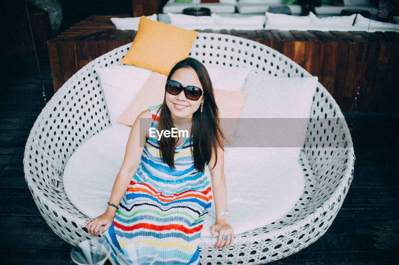 High angle portrait of smiling woman wearing sunglasses sitting on chair