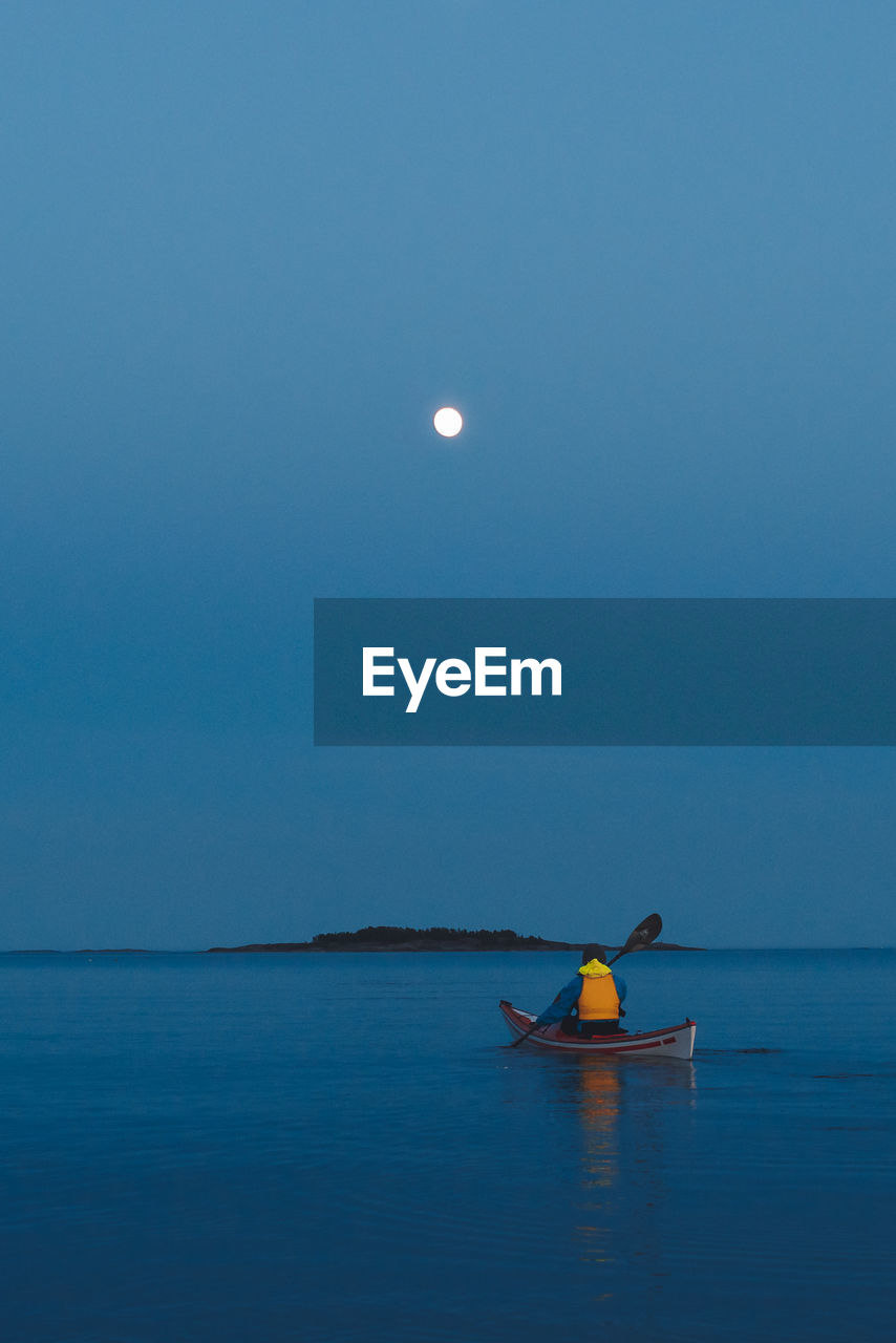 A kayaker paddles towards the moon.