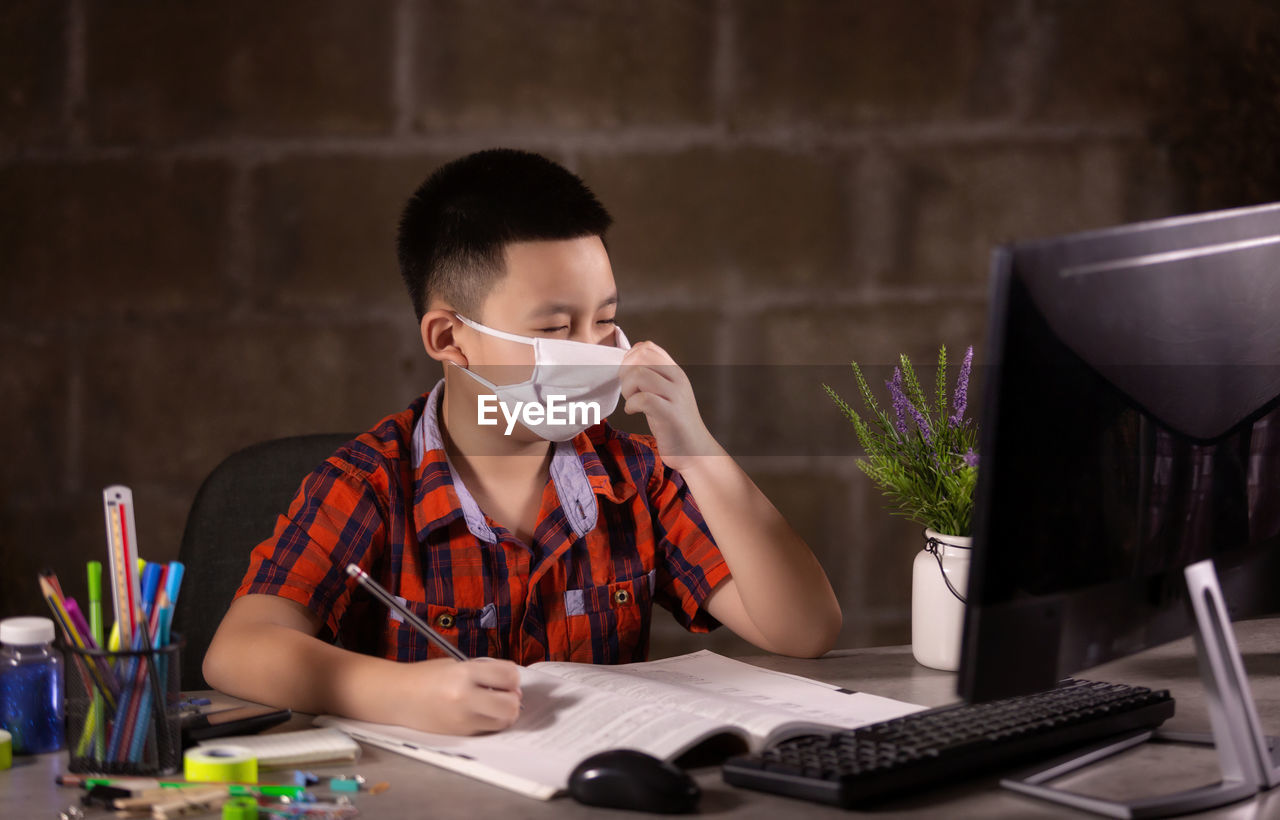 Happy boy studying with face mask on table at home