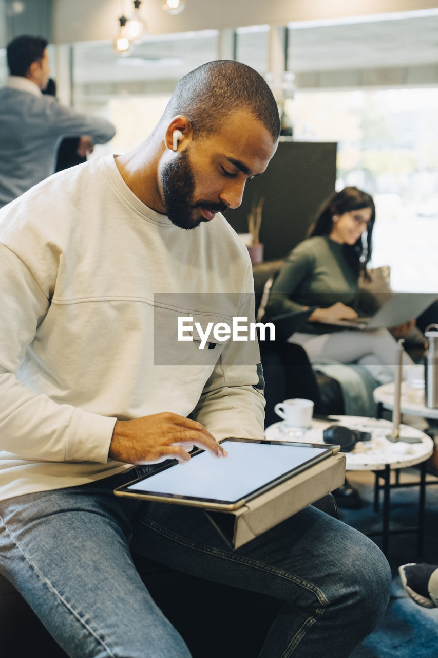 Male entrepreneur using digital tablet while working with colleagues in office