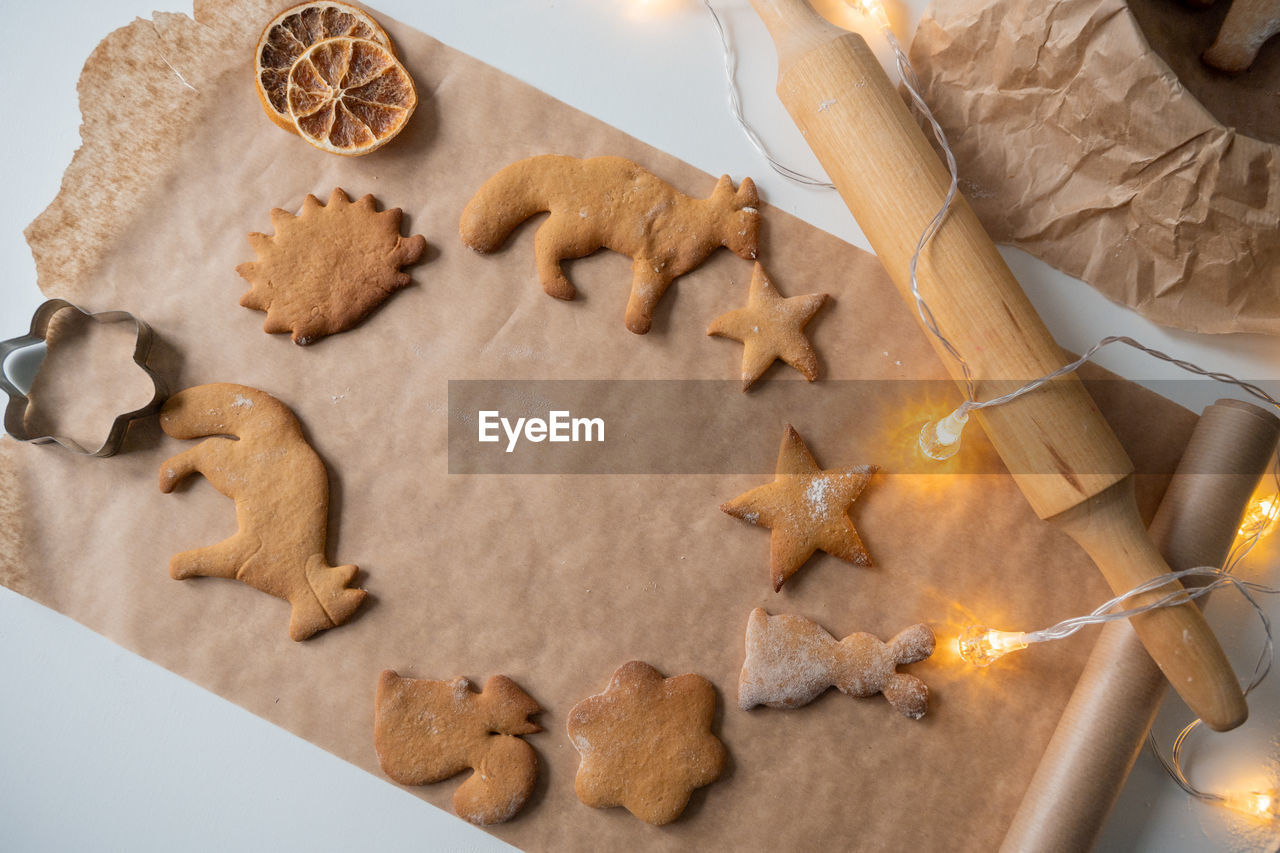 A frame of ginger cookies of different shapes on parchment, a rolling pin on the table and garlands