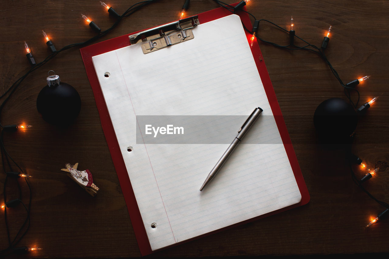 High angle view of illuminated string light by lined paper on clipboard at table