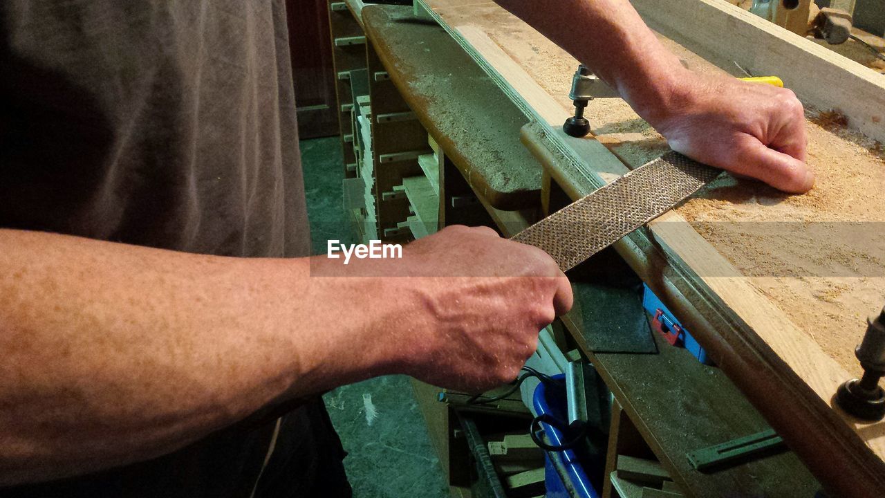 Midsection of carpenter using rasp at workshop