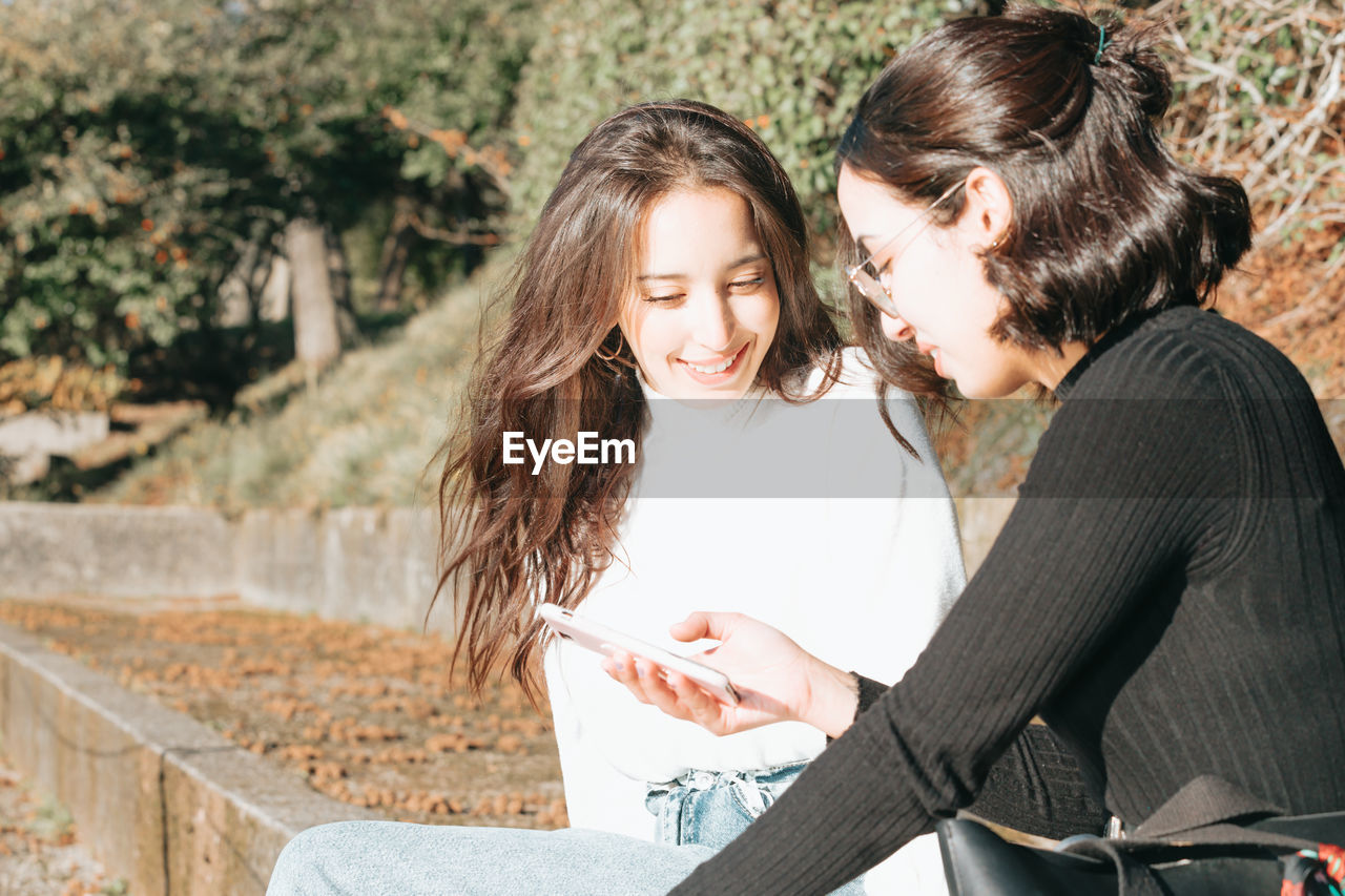 Smiling female friends looking at mobile phone