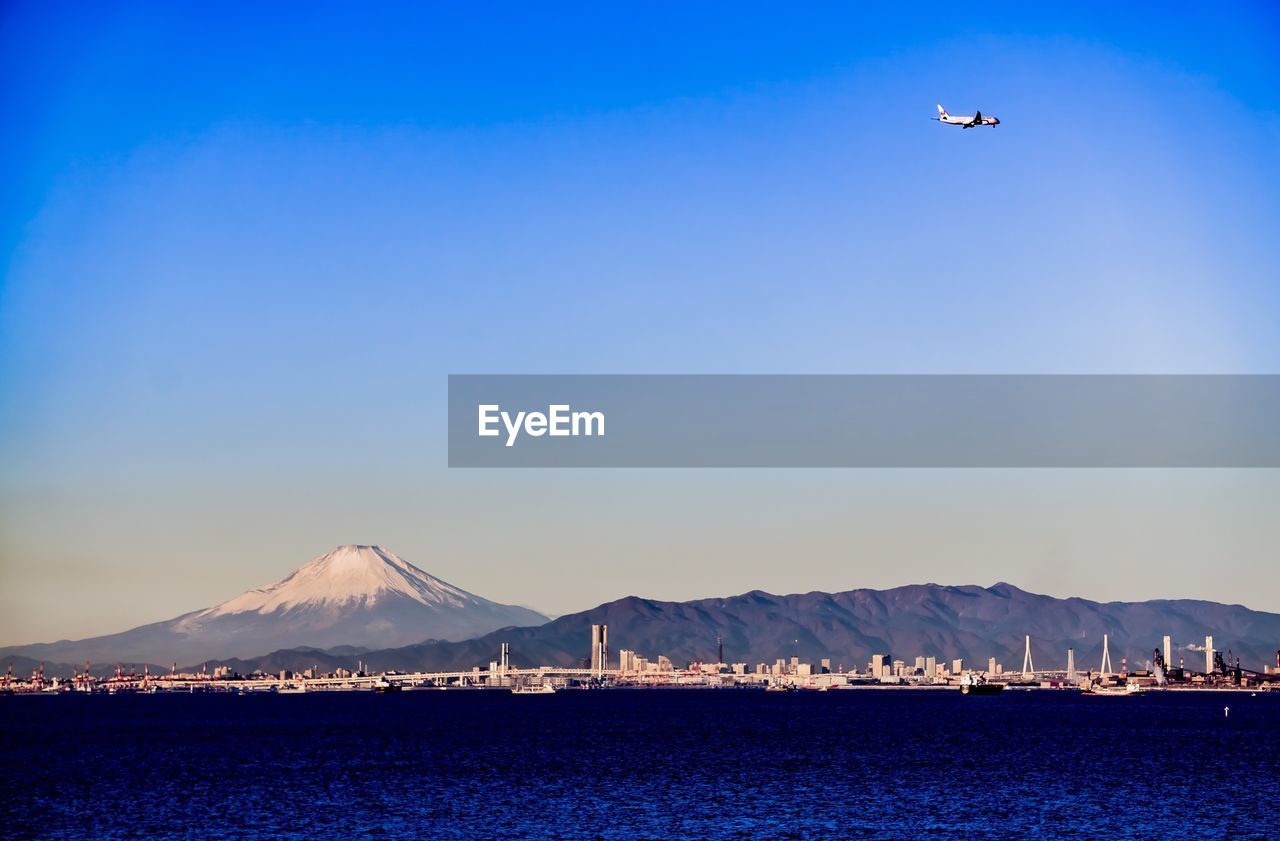 AIRPLANE FLYING OVER SEA AGAINST BLUE SKY